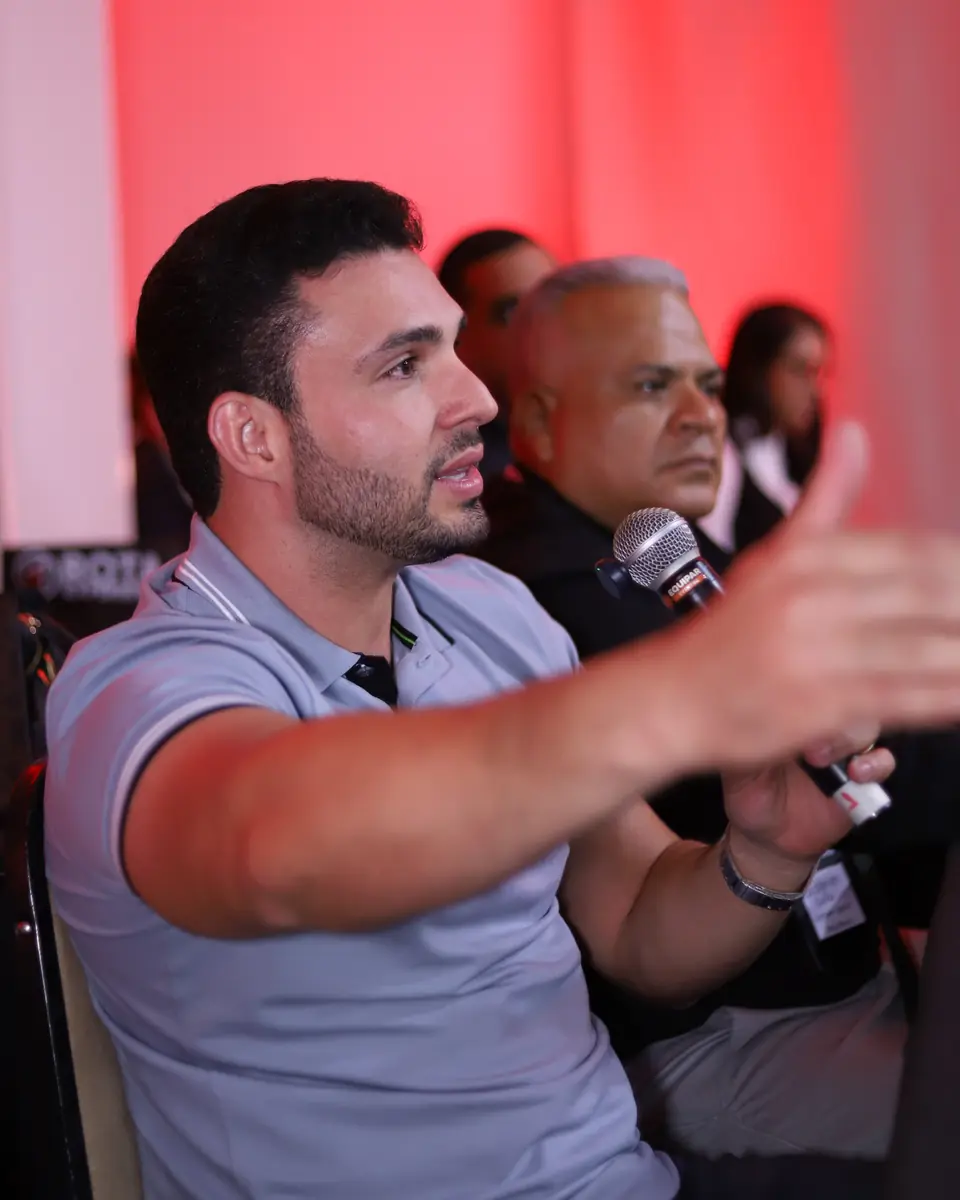 Participante com o microfone na mão fazendo uma pergunta à mesa