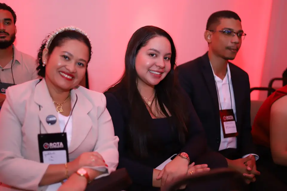 Três participantes sorrindo lado a lado na plateia do ROTA EXPERIENCE